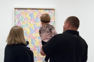 A couple holds a toddler while looking at a colorful artwork