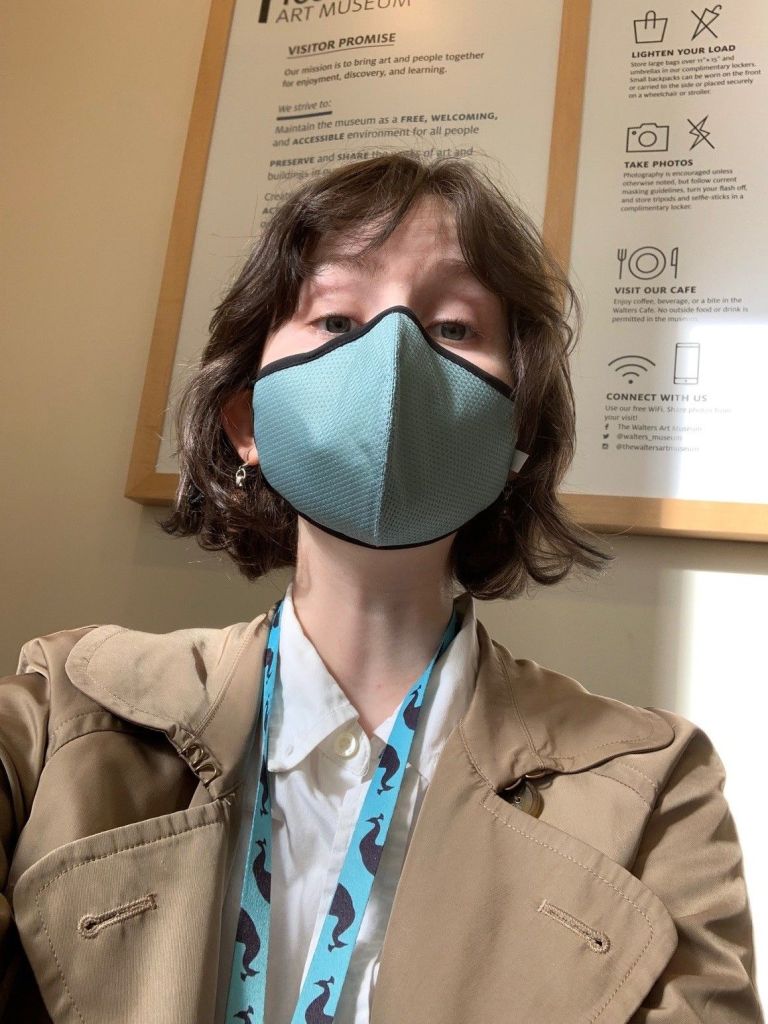 A person wearing a face mask and a badge lanyard in front of a sign with notes and instructions for visitors