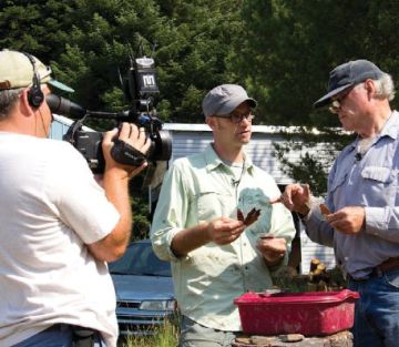 Image of three men discussing a leaf while on camera (one of the men is a cameraman). 