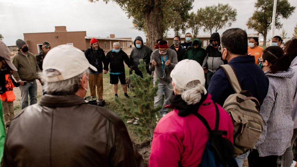 A circle of people watching someone say a blessing over a tree