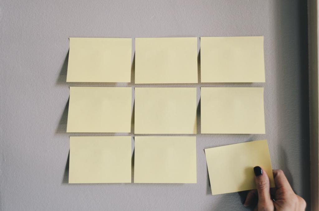 A grid of sticky notes on a wall with a hand reaching up to place one