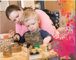 A mother and son look at some building materials in front of them on a table.