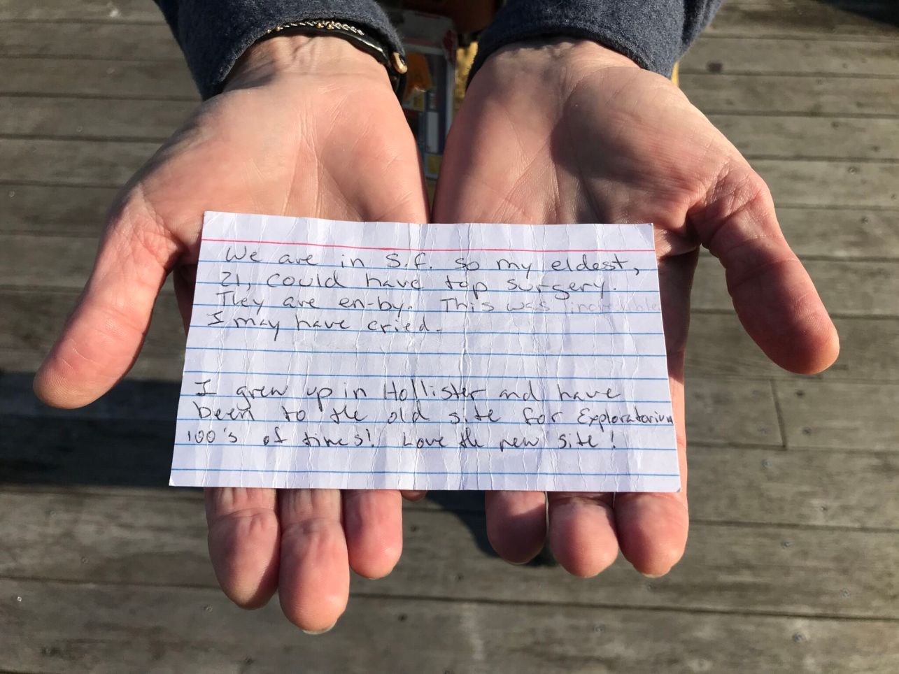Two hands hold a handwritten lined note card with a comment about the exhibition.