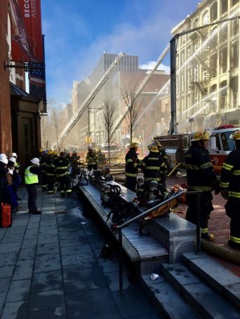 A group of firefighters stand with water hoses shooting water toward a building.