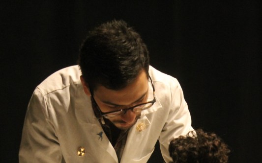 An educator wearing a lab coat standing with a young student
