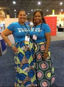 Two people posing for a portrait wearing t-shirts that say "Museums & Race," African print skirts, and conference badges.