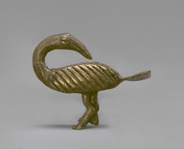 A small brass sculpture of a stylized bird with its neck turned around to face its tail feather.