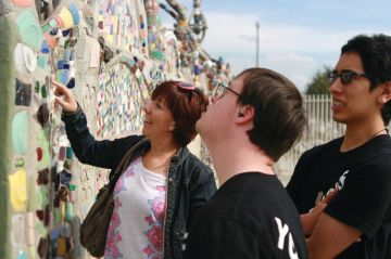 Three people look at a colorful mosaic wall.
