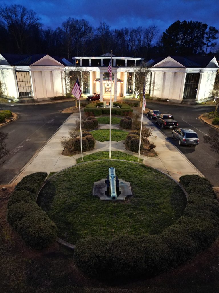 Exterior of the museum, lit at night with front greenery in the drive up to the entrance.