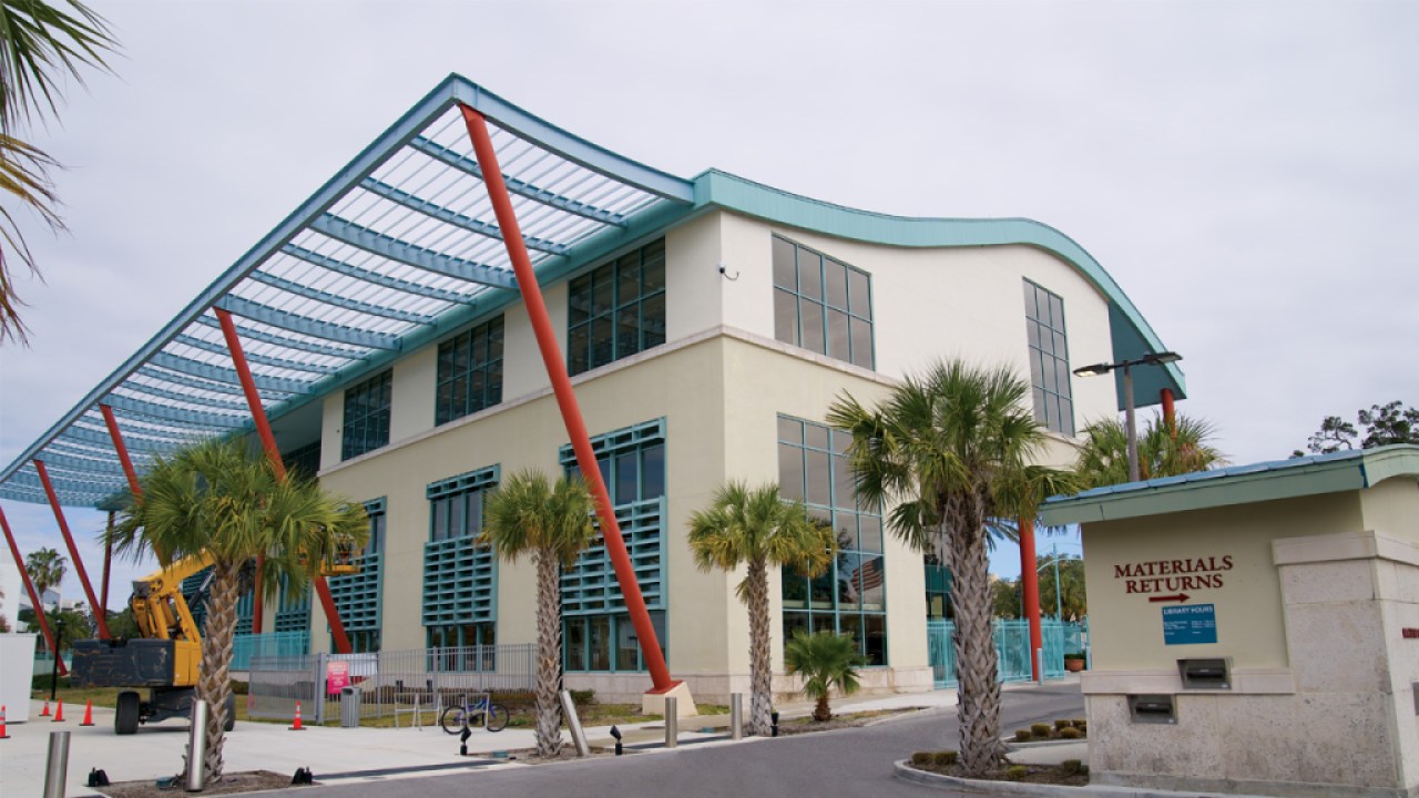 An exterior view of a municipal building with a structure in front of it reading "materials returns" with an arrow symbol