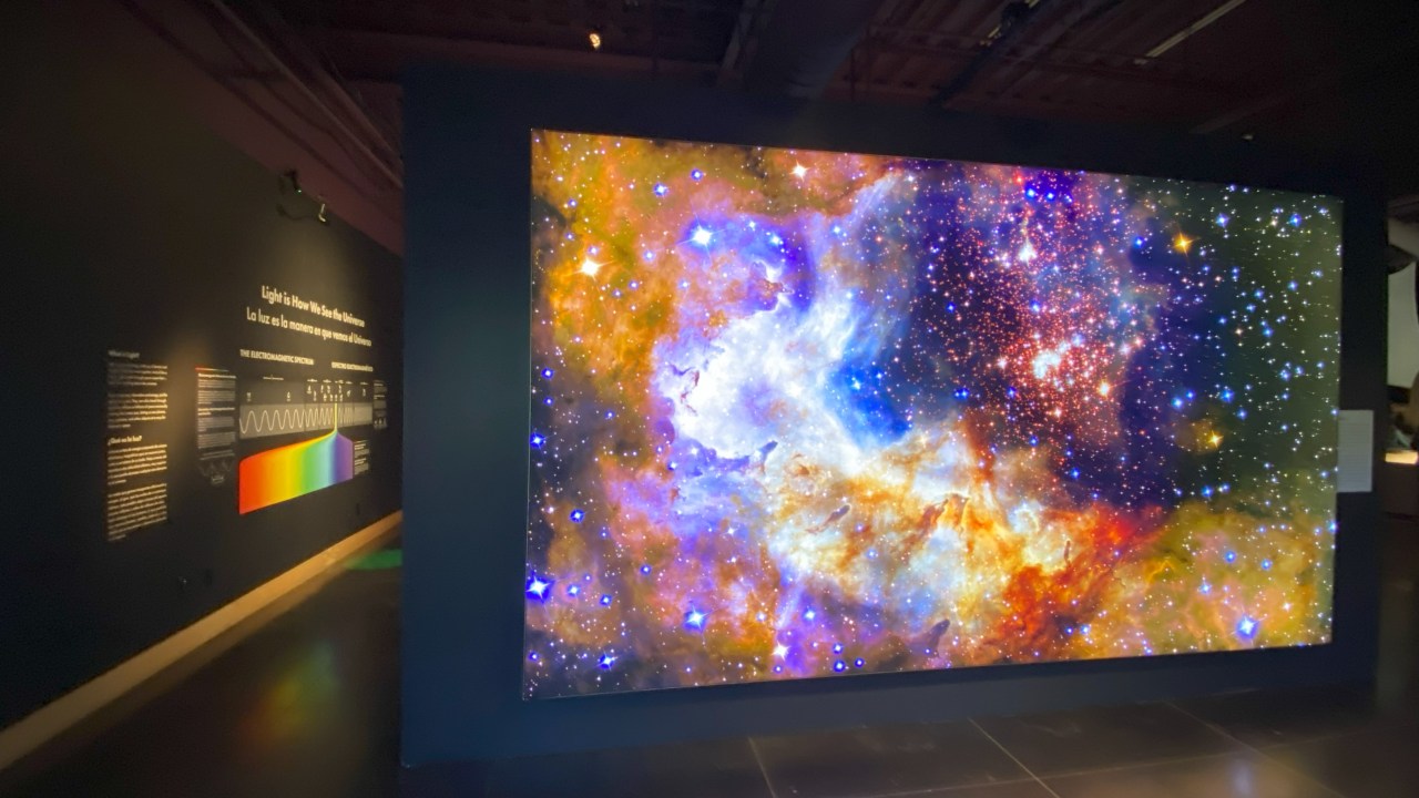 Interior of visitor center with a multi-colored view of a galaxy on a dark colored wall.