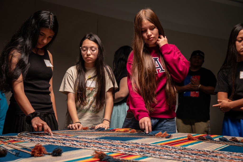 A group of children, descendents of Muscogee (Creek) Nation interact with vibrantly colored woven material.