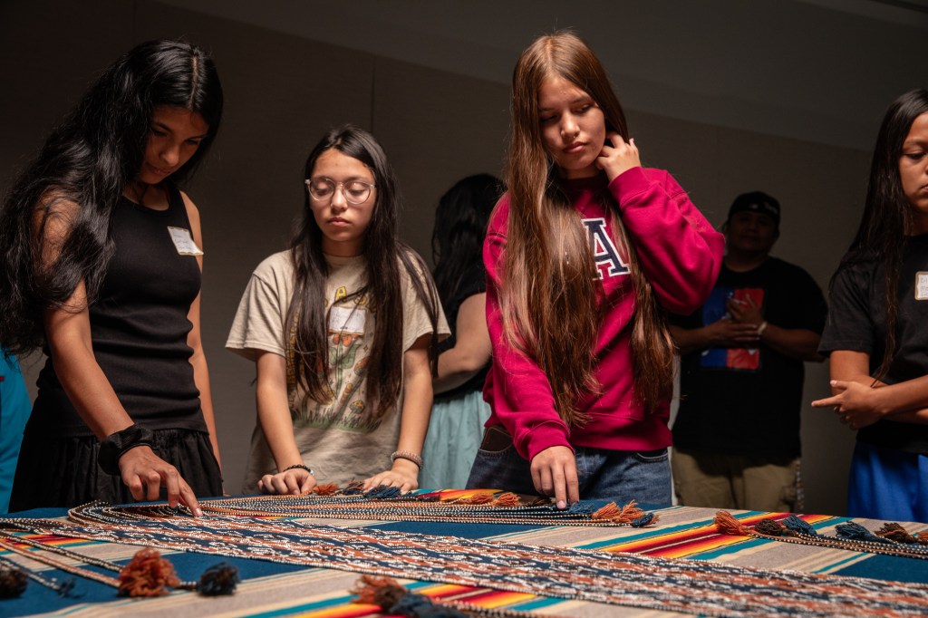 A group of children, descendents of Muscogee (Creek) Nation interact with vibrantly colored woven material.