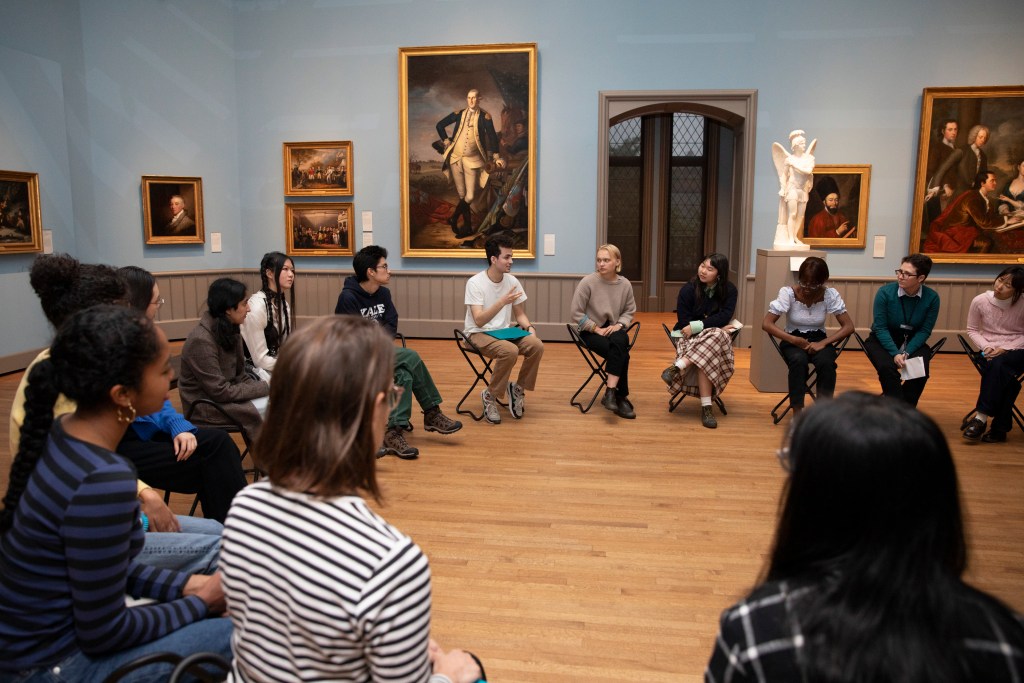 A group of people seated in a circle on folding chairs in a museum gallery