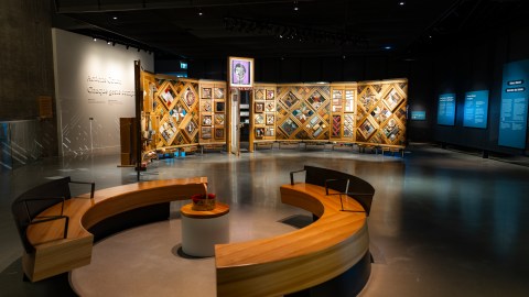 Exhibition with large room space, focus is a textile patchwork wall and circular seating around another object.