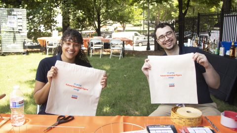 Two young people posing with tote bags reading "it's giving future historical figure energy" with the civic season logo beneath it