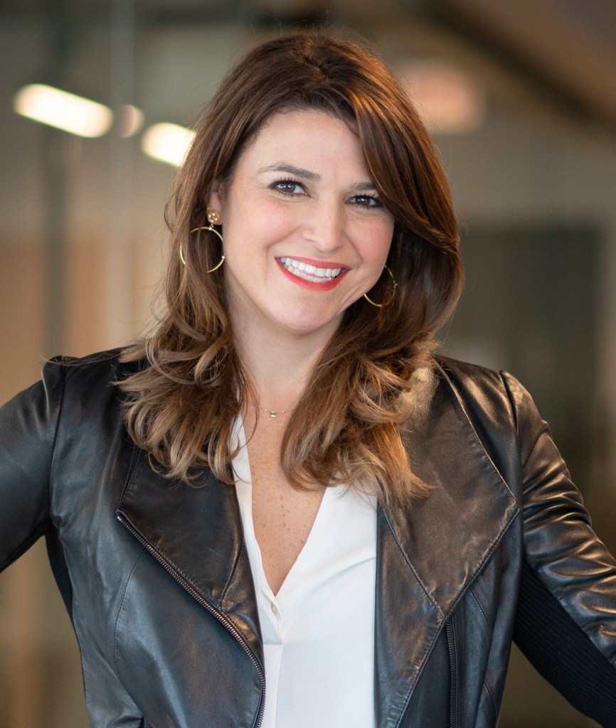 Photo of AJ Goehle. She is standing and smiling with brown hair.