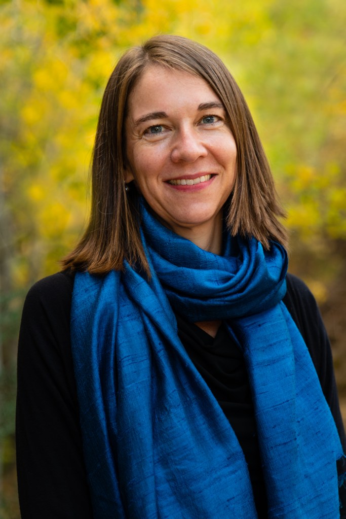 Photo of Dana Whitelaw. She is standing with short light brown hair and smiling.