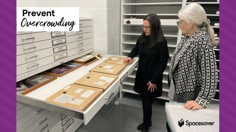 Two people stand next to a map file cabinet with one drawer pulled open.