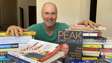A person sitting down behind a pile of books