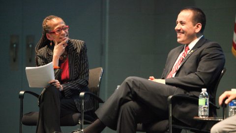 Two seated speakers smiling on stage