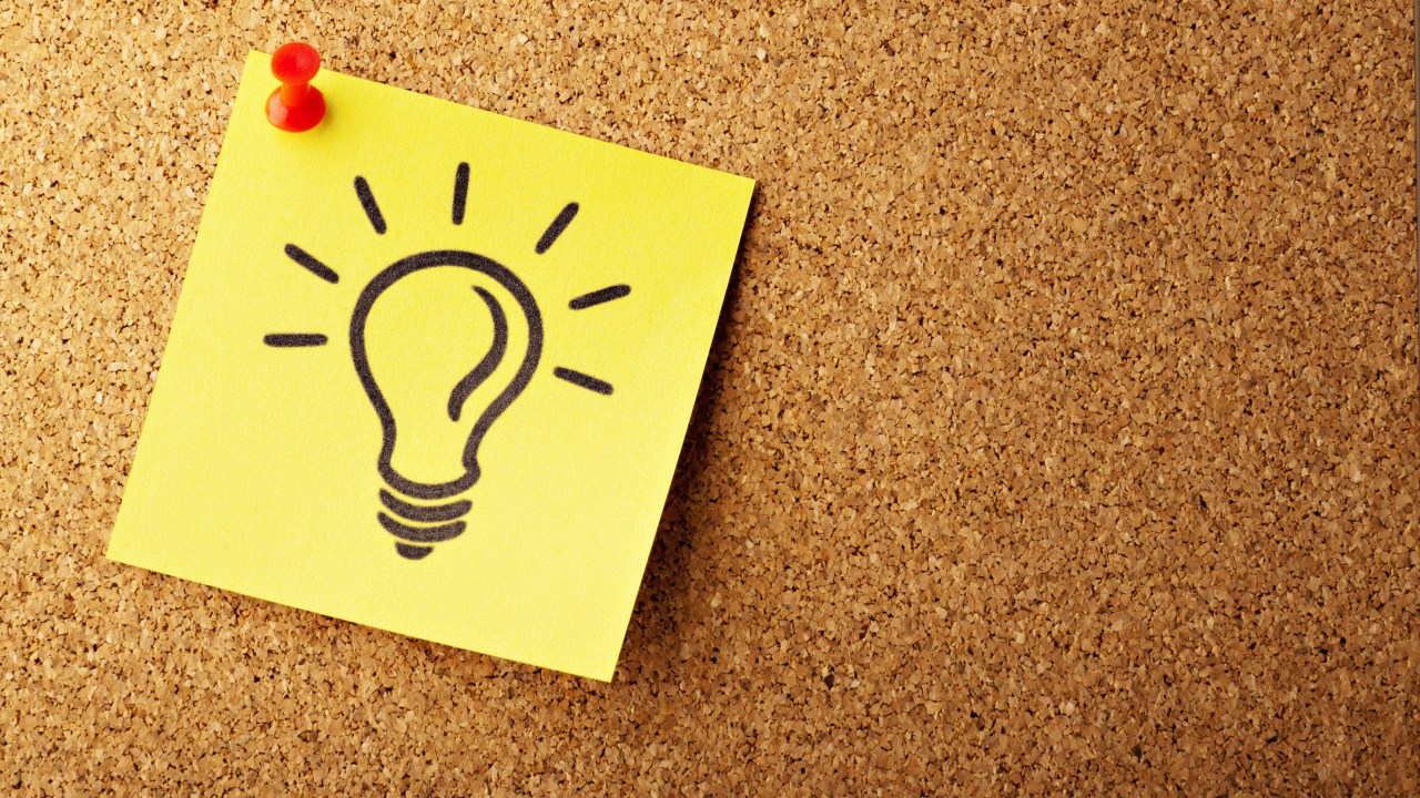 A post-it note with a drawn lightbulb is pinned to a corkboard.