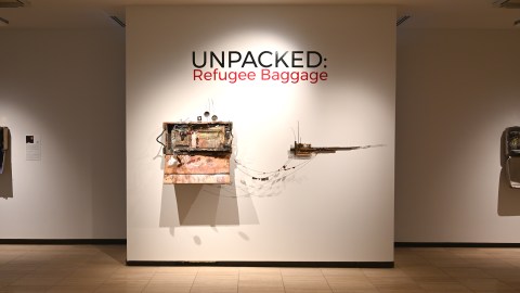 Title of the exhibit Unpacked: Refugee Baggage on a museum wall with art work on below and on either side of the title.