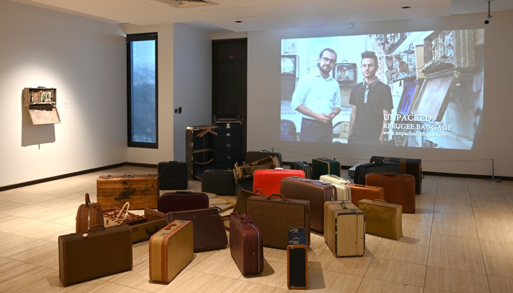 Suitcases in front of a video as part of the Unpacked: Refugee Baggage exhibition.