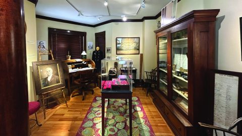 A room with exhibits of a historical society, from wooden case displays to a frame portrait.