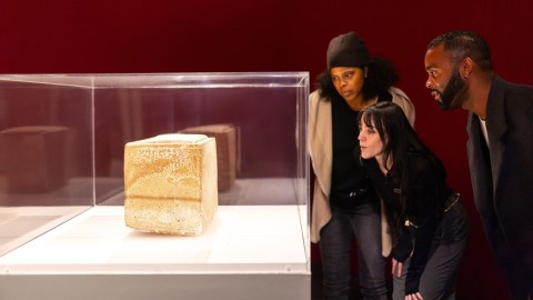 A group of visitors gaze at a 1st-century limestone burial box displayed inside a vitrine.