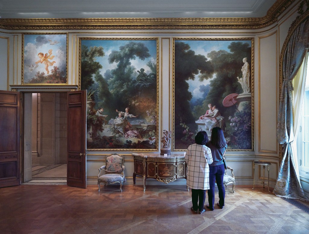 Two visitors with their backs to the camera view paintings on display in The Frick's Fragonard Room.