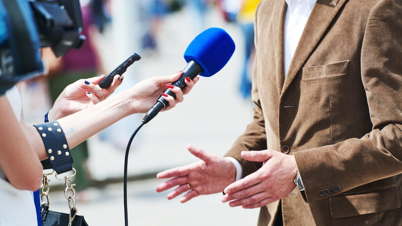 Journalists holding up microphones to a person speaking