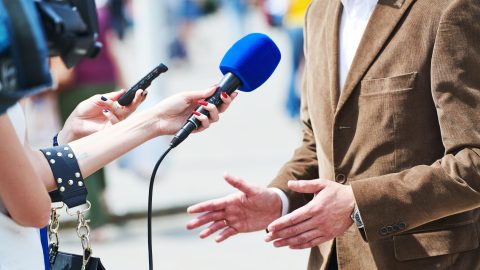 Journalists holding up microphones to a person speaking