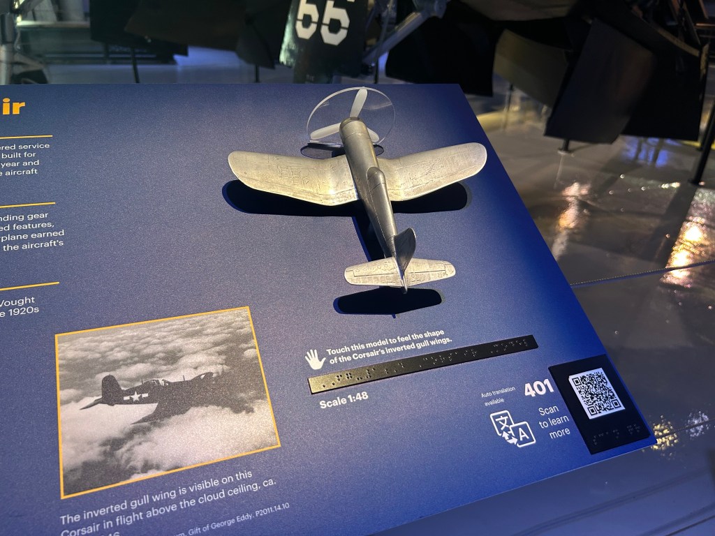 A aluminum-cast model of an airplane invites visitors to touch it as part of that object's label. The label also includes a photograph of the plane in flight and a translation in braille.