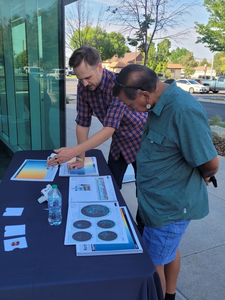 Two men outside look at a table with different booklets.