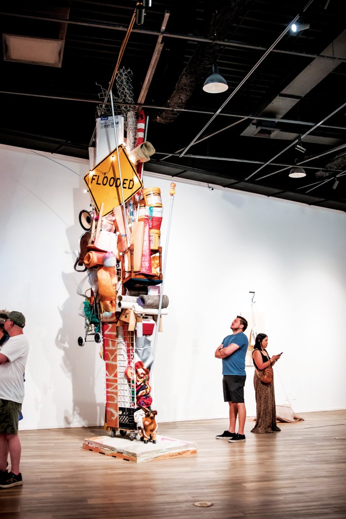 A giant found objects sculpture in a gallery with visitors.