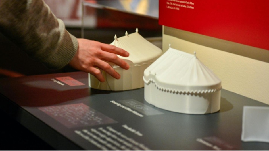 A close-up of a visitor touching one of the 3D-printed tent replicas. 
