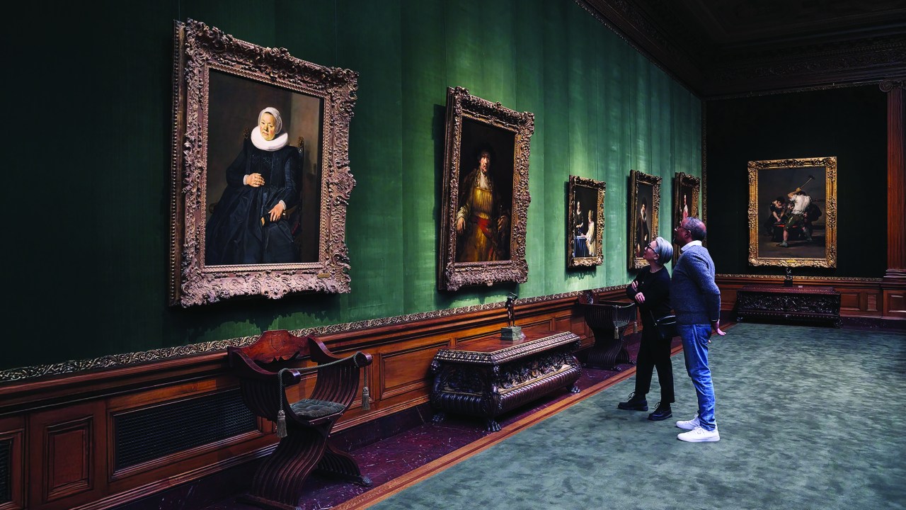Two visitors stand in front of a painting inside a gallery at The Frick Collection.