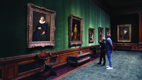 Two visitors stand in front of a painting inside a gallery at The Frick Collection.