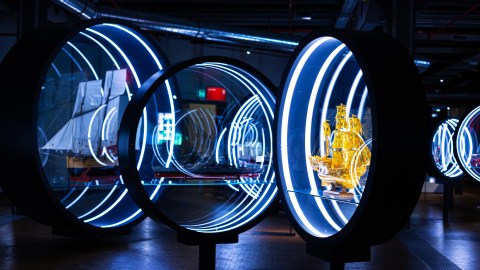 An installation of three ship models inside round vitrines with neon lights on them