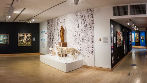 Museum exhibition showing a wooden statue and two wolves in front of a wall with an image of a snowy forest
