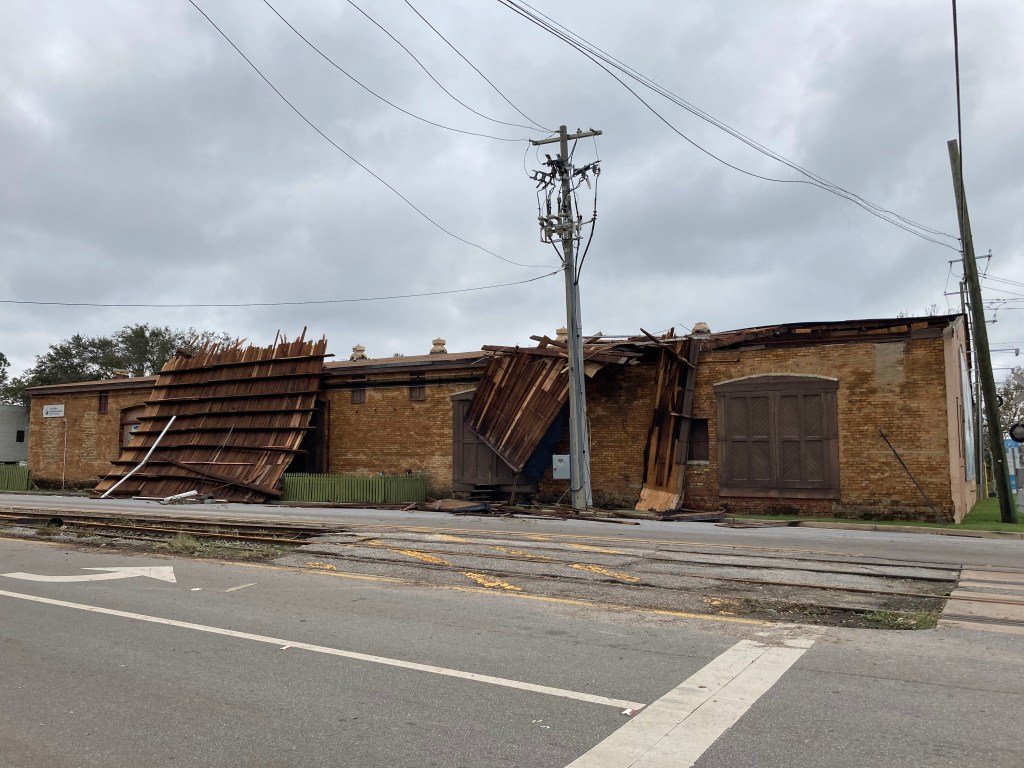 A large piece of the Museum of Commerce roof is vertical in front of the building with loose powerlines around.