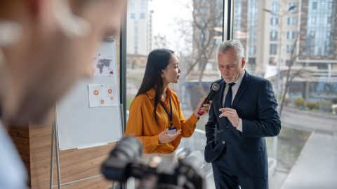 A journalist interviewing a person in a suit with a microphone