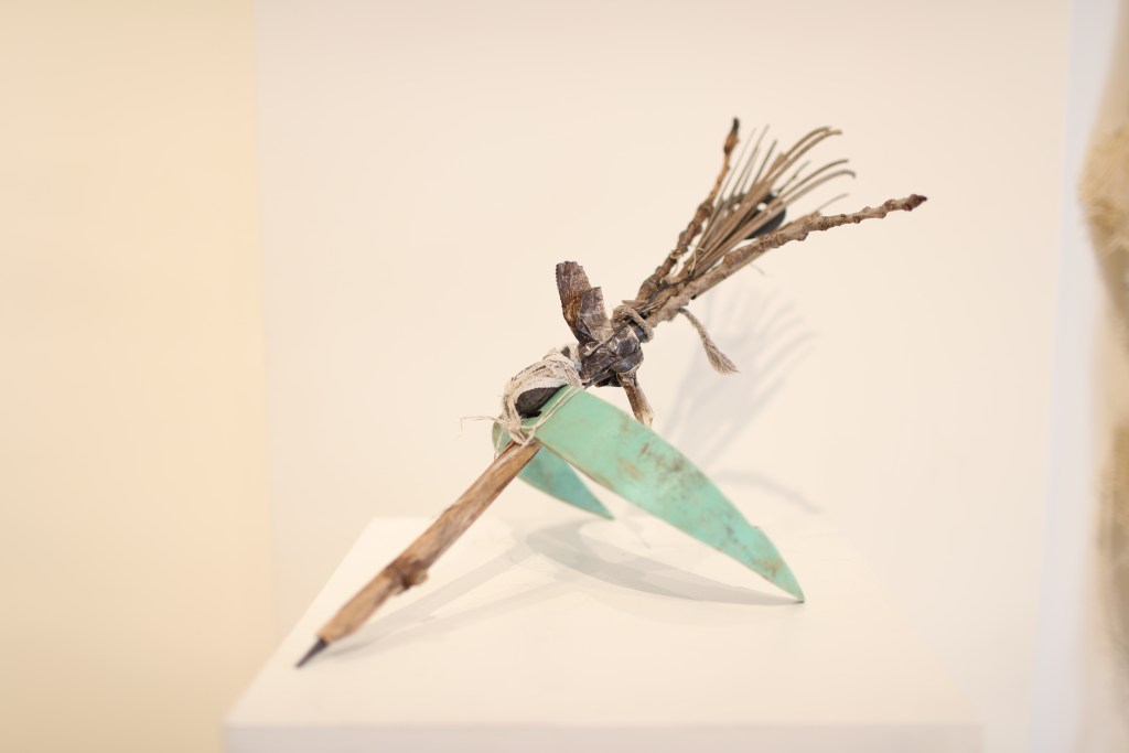 The artifact, "Storycatcher" which is a pen with twigs coming out the end and green wings coming out the sides.