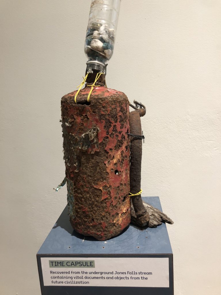 A plastic water bottle filled with rocks pouring into a rusted fire extinguisher.