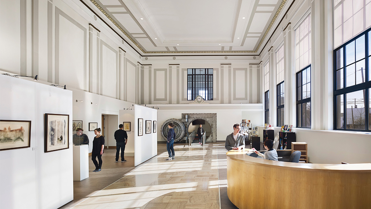 Big space with white walls with art on them and a reception desk in the front.