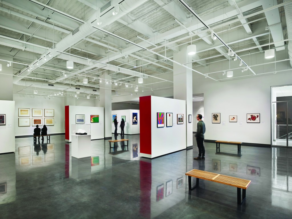People standing in large space looking at artworks on the walls. The walls are modular and can be moved.