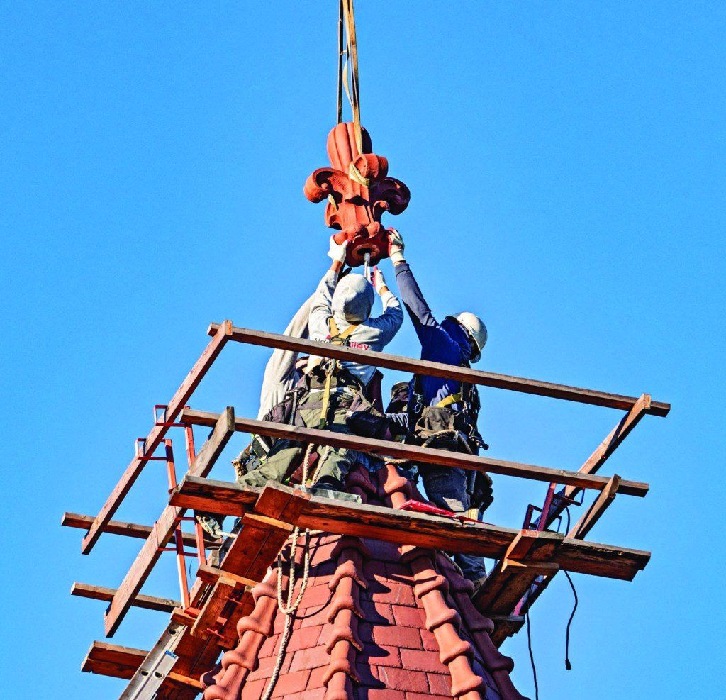 construction workers installing a red finial on top of a pointy tower.