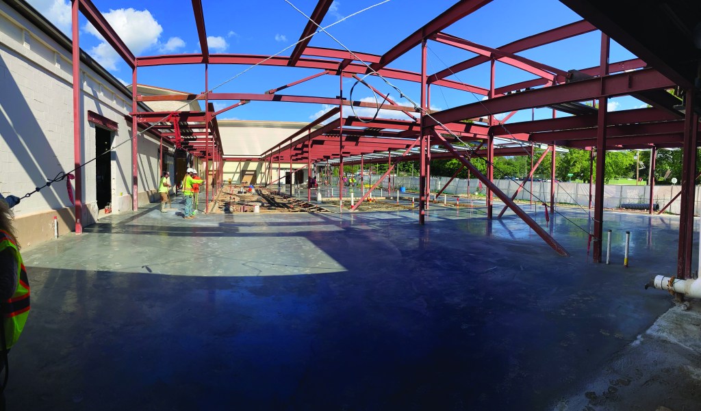 Construction workers pouring concrete around metal framing for an building addition.