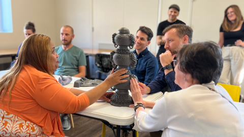 A group of people sit around a table with a bronze sculpture touching and examining it closely.